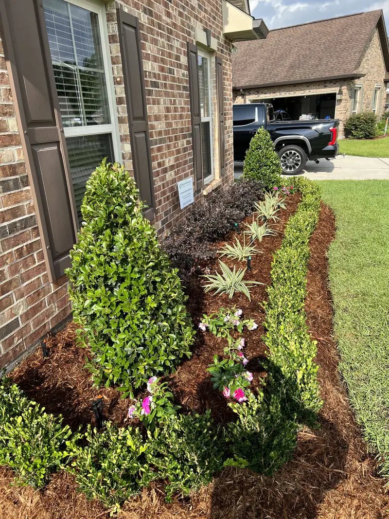 Mulched garden bed with shrubs and flowers along a brick home.